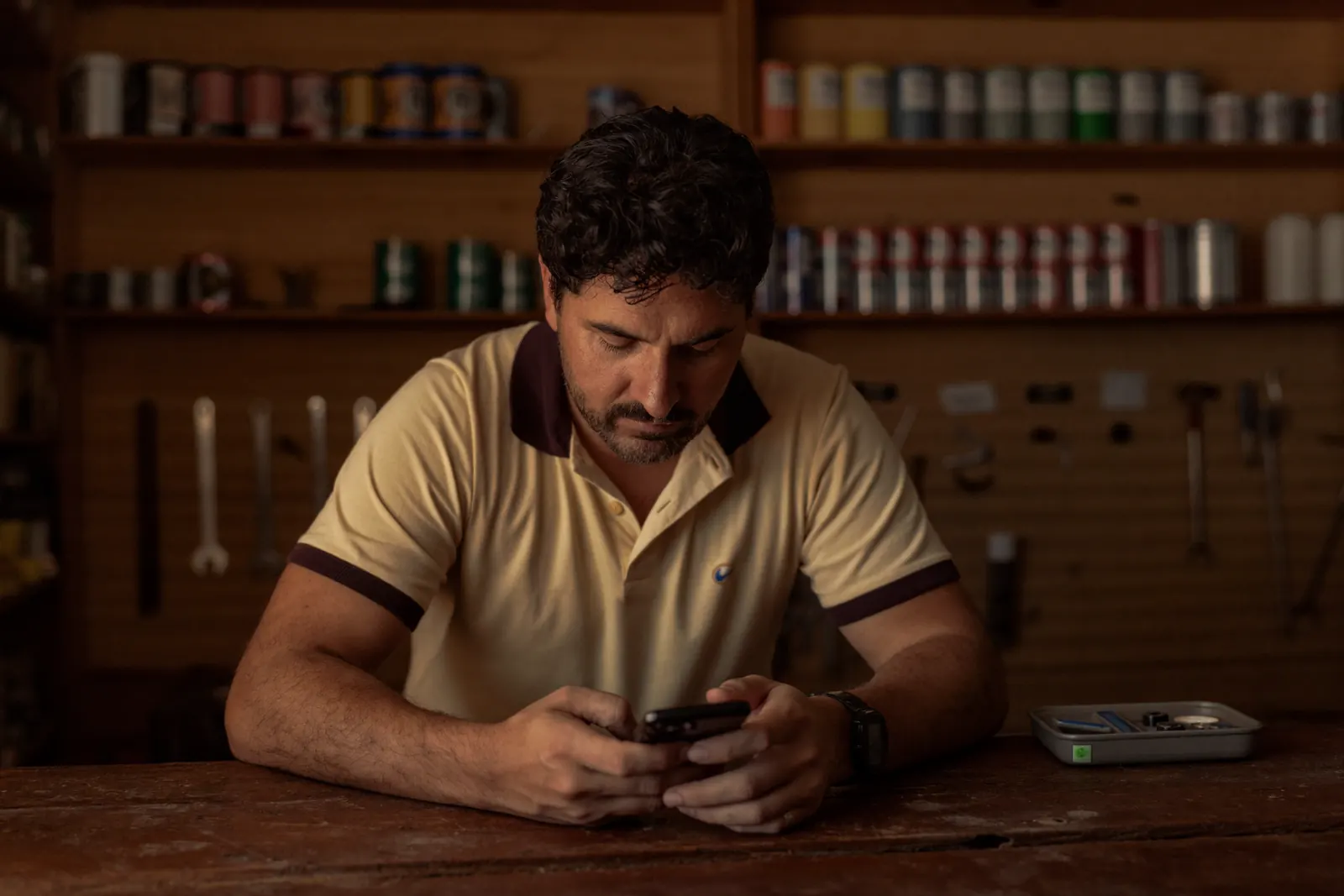 Dono de loja de material de construção atrás do balcão, olhando o celular